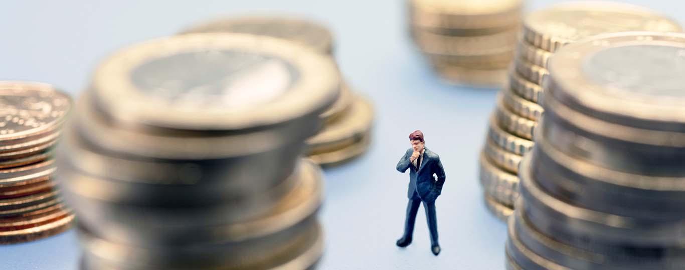 istock by Getty Images mannetje kijkt bedenkelijk tussen opgestapelde munten