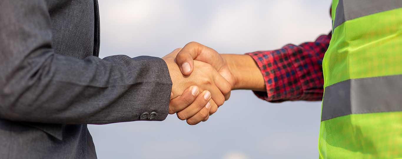 Sociaal overleg: iemand in maatpak en in geel vestje schudden elkaar de hand 