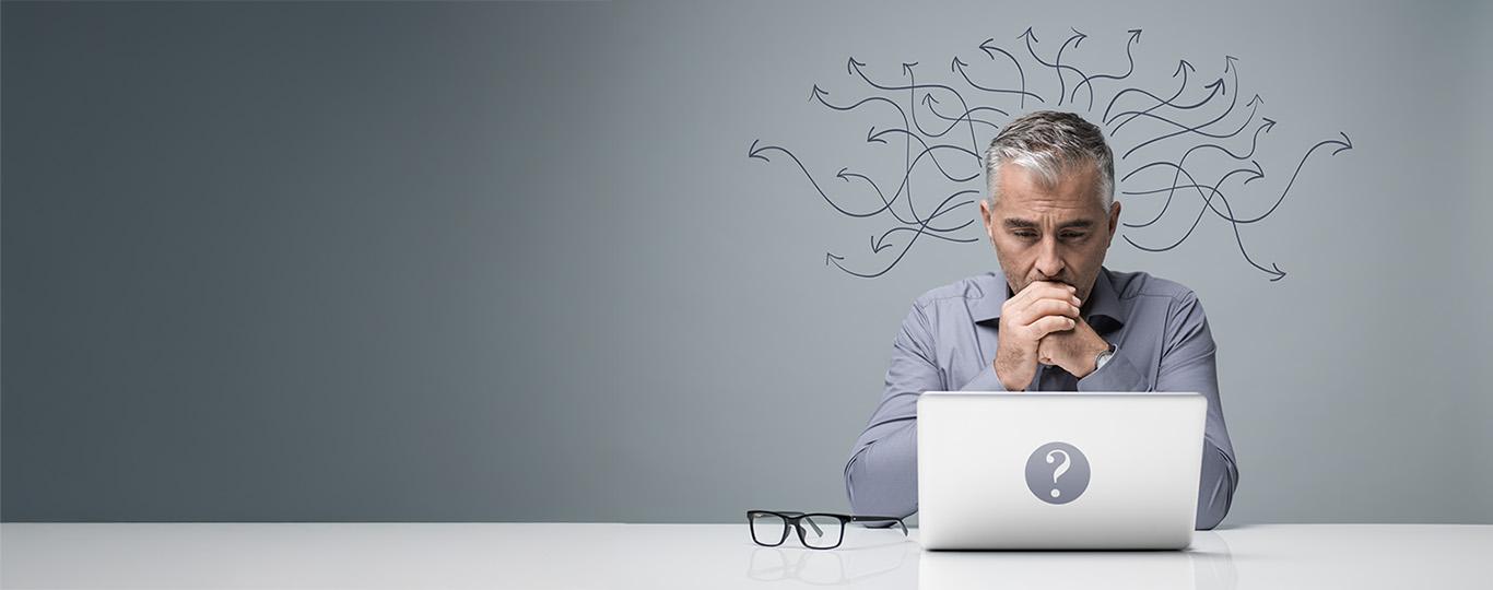 man kijkt bedenkelijk naar zijn laptop, boven zijn hoofd staan pijken die alle richtingen uitgaan