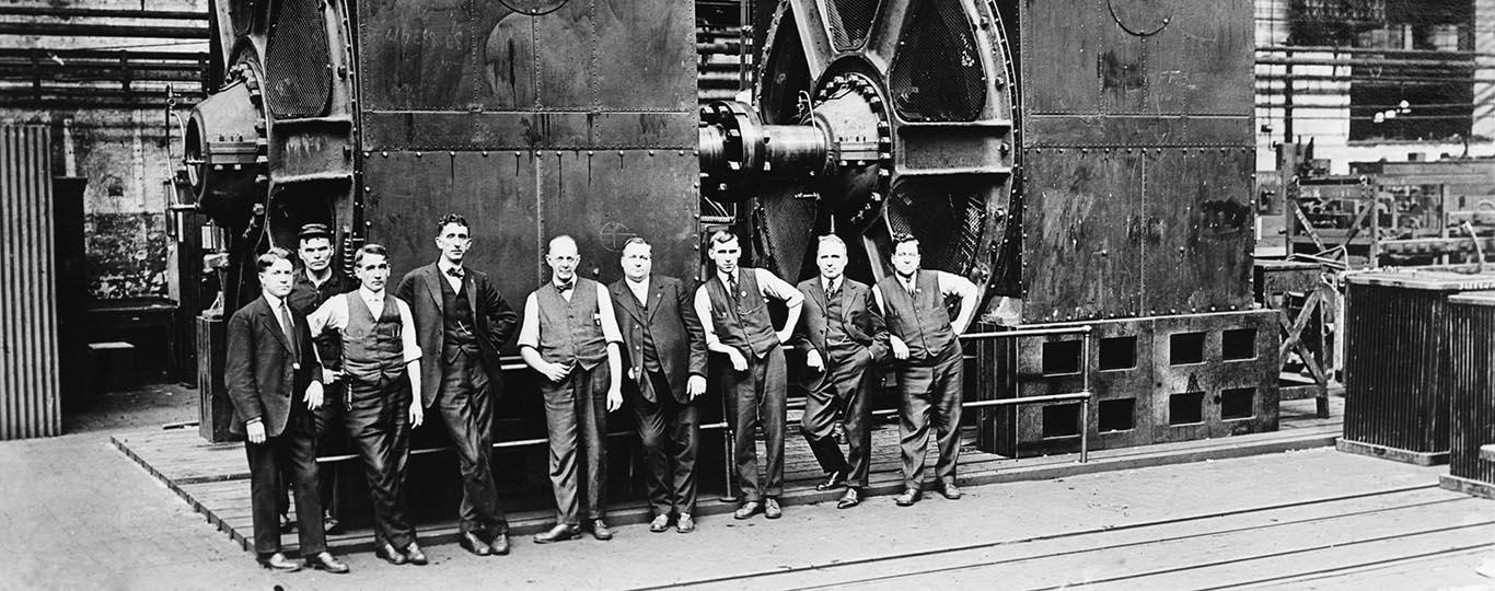 arbeiders en directieleden voor een stoommachine in een oude fabriek