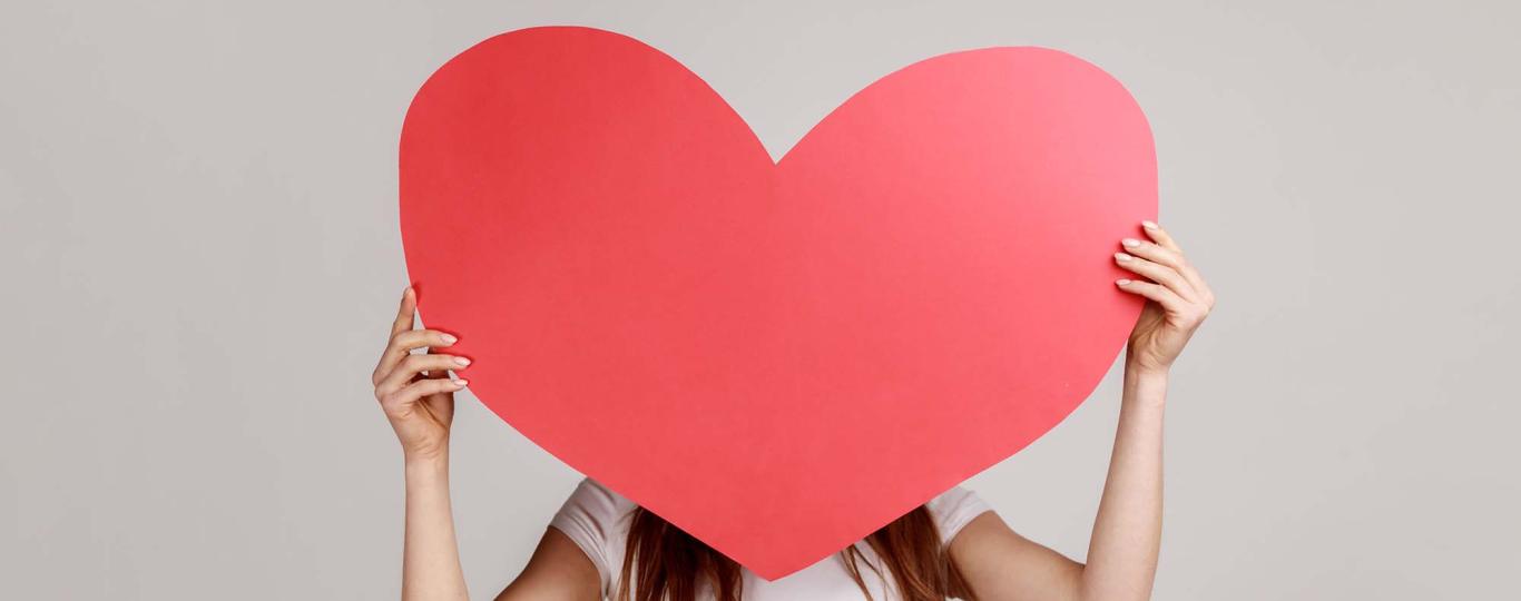 jonge vrouw houdt groot papieren hart voor haar gezicht