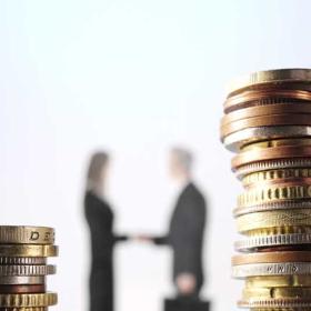 stijgende loonkosten: man en vrouw schudden elkaar de hand tussen stapels euromunten