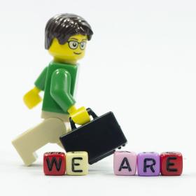 lego-mannetje met aktentas stapt voorbij letterblokjes die de zin we're hiring vormen