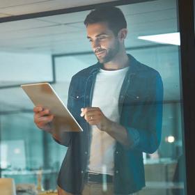man in modern kantoor kijkt glimlachend naar tablet