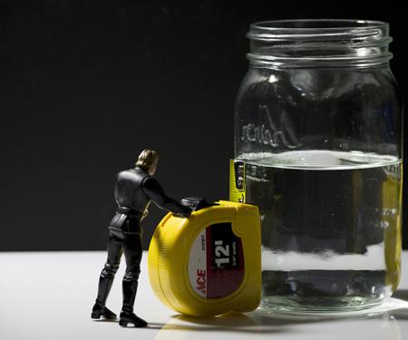 Miniatuur mannetje meet de inhoud van een halfvol glas