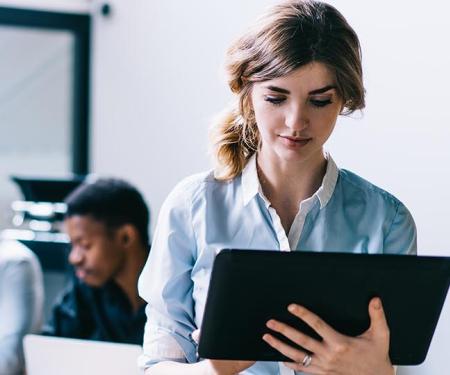 vrouw zoekt info op tablet, met teamgenoten op achtergrond