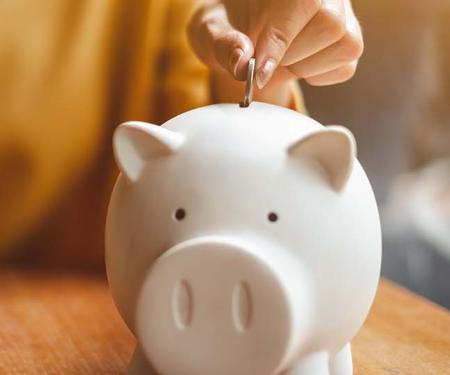 vrouw aan bureau steekt geld in spaarvarken