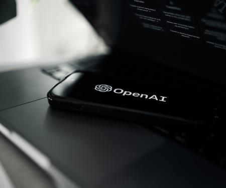 logo open ai op een smartphone liggend op een half opengeklapte laptop