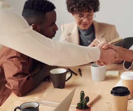 2 mensen schudden de hand met op de achtergrond 2 collega's in gesprek
