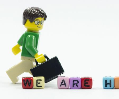 lego-mannetje met aktentas stapt voorbij letterblokjes die de zin we're hiring vormen