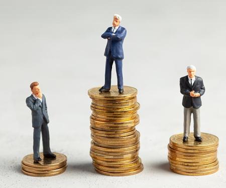 3 miniatuurmannetjes in maatpak staan op stapeltjes geld van verschillende hoogte