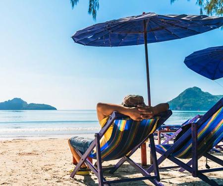 ontspannen jonge man in een strandstoel kijkt voor zich uit over de zee naar een eilandje