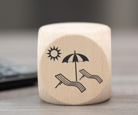 dobbelsteen met daarop een afbeelding van 2 strandstoelen in de zon ligt op een tafel naast een calculator