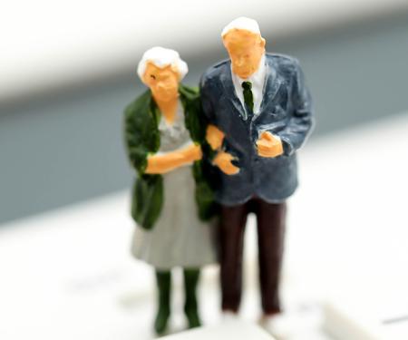 ouder koppel miniatuurpoppetjes staat op rekenmachine met daarop een toets tax min en plus