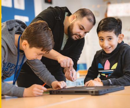 docent helpt twee kinderen met laptop